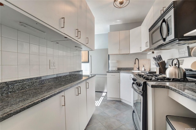 kitchen with sink, stainless steel appliances, dark stone countertops, decorative backsplash, and white cabinets