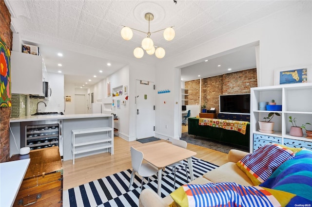 living room with brick wall, beverage cooler, sink, a notable chandelier, and light hardwood / wood-style floors