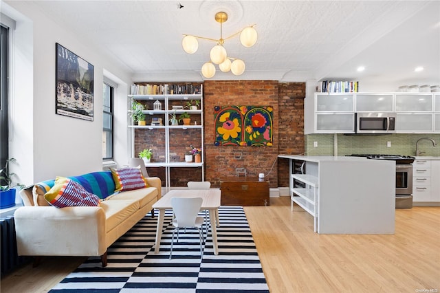 living room featuring an inviting chandelier, sink, a textured ceiling, light hardwood / wood-style floors, and brick wall