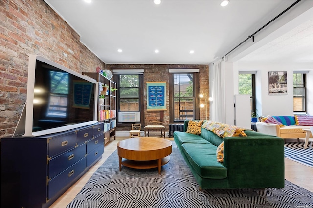 living room featuring wood-type flooring, radiator heating unit, and brick wall