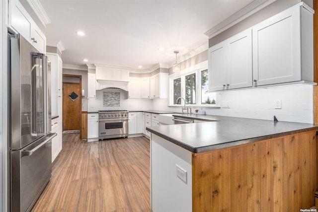 kitchen with pendant lighting, high quality appliances, white cabinets, crown molding, and kitchen peninsula