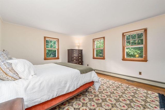 bedroom featuring baseboard heating, wood-type flooring, and ornamental molding