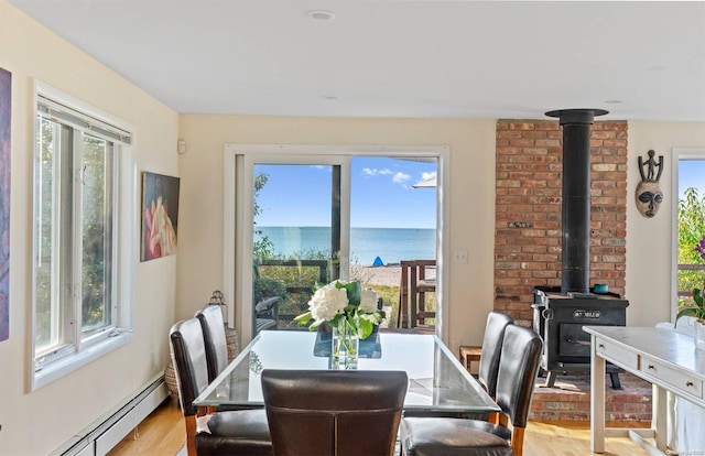 dining space featuring baseboard heating, a wealth of natural light, light hardwood / wood-style flooring, and a water view