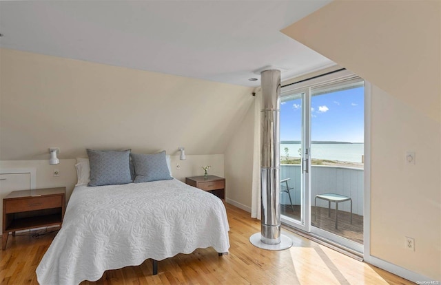 bedroom featuring access to exterior, a water view, vaulted ceiling, and hardwood / wood-style flooring