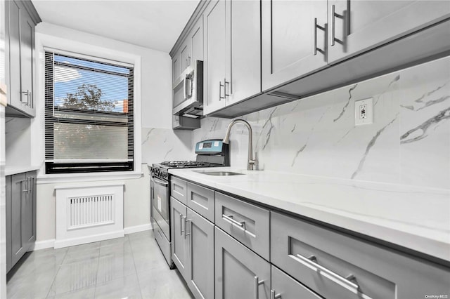 kitchen featuring sink, decorative backsplash, gray cabinets, light stone counters, and stainless steel appliances