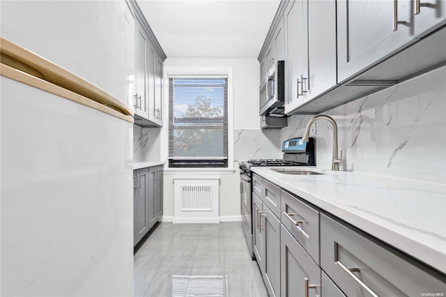 kitchen with sink, decorative backsplash, gray cabinets, light stone countertops, and stainless steel appliances