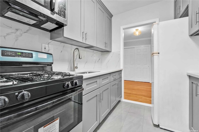 kitchen featuring gas stove, gray cabinetry, sink, white fridge, and decorative backsplash