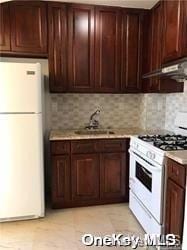 kitchen with dark brown cabinets, decorative backsplash, sink, and white appliances