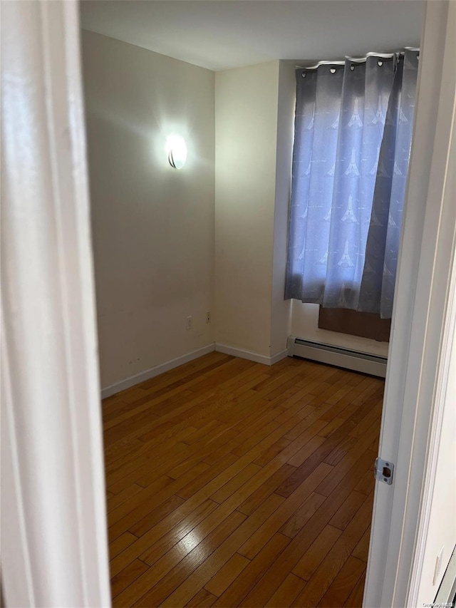 unfurnished room featuring wood-type flooring and a baseboard radiator