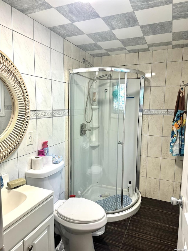 bathroom featuring vanity, a shower with door, tile walls, tile patterned flooring, and toilet