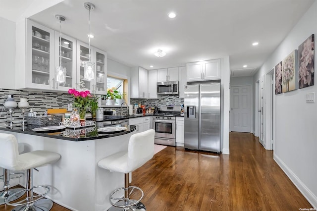 kitchen with white cabinets, stainless steel appliances, hanging light fixtures, and dark wood-type flooring