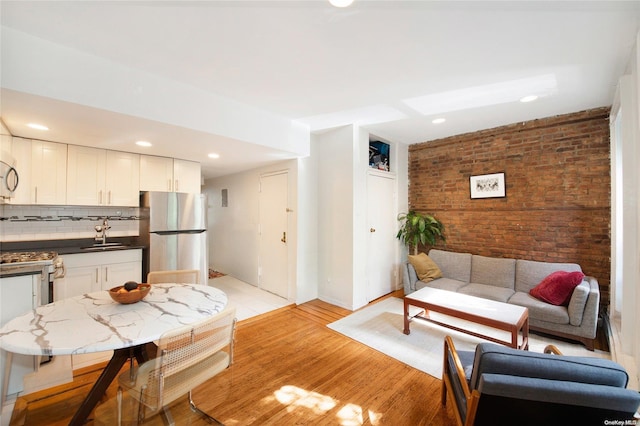 living room with sink, brick wall, and light wood-type flooring