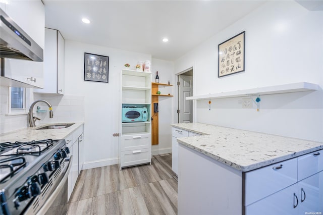 kitchen featuring tasteful backsplash, light stone counters, wall chimney exhaust hood, light hardwood / wood-style flooring, and white cabinets