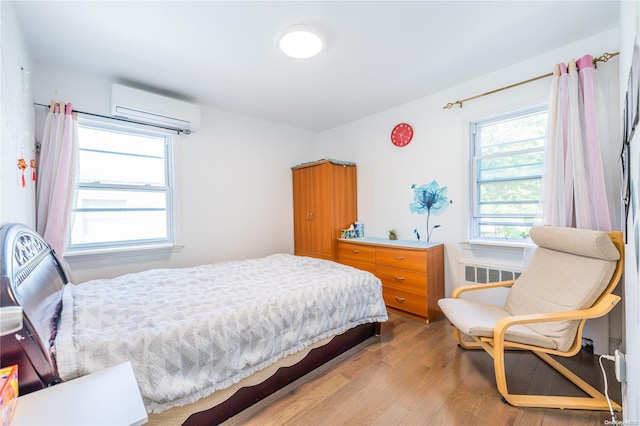 bedroom with radiator heating unit, light hardwood / wood-style floors, and a wall unit AC