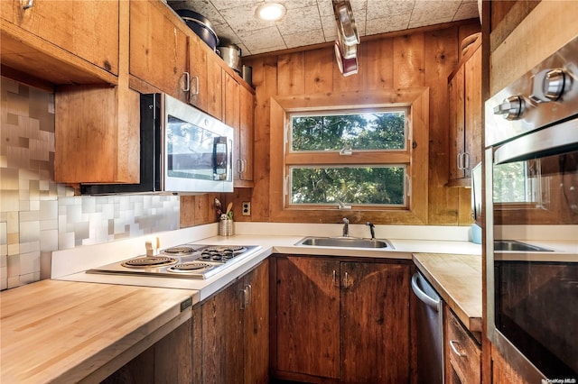 kitchen featuring sink, wooden counters, backsplash, wooden walls, and appliances with stainless steel finishes