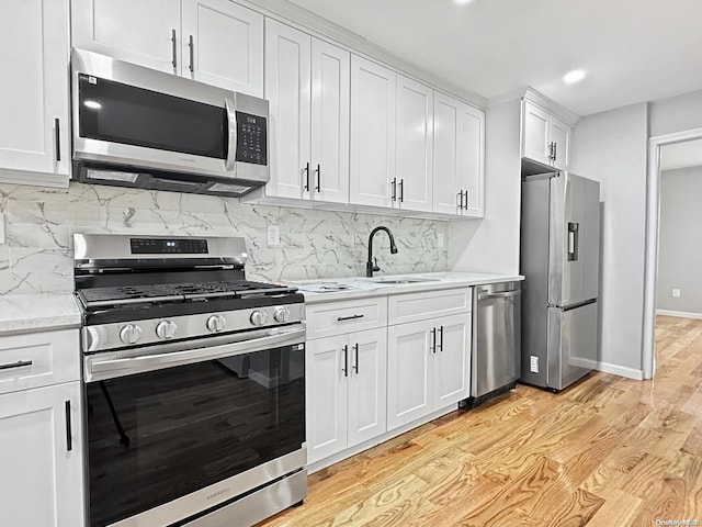 kitchen featuring decorative backsplash, appliances with stainless steel finishes, sink, white cabinets, and light hardwood / wood-style floors