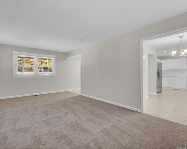 spare room featuring light colored carpet and a chandelier