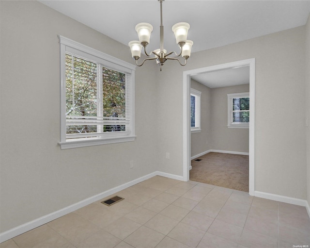 tiled spare room featuring plenty of natural light and an inviting chandelier