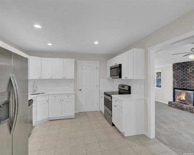 kitchen with sink, light colored carpet, a fireplace, white cabinets, and appliances with stainless steel finishes