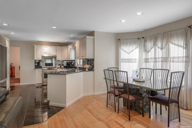 kitchen featuring hardwood / wood-style floors, backsplash, white cabinets, sink, and stainless steel stove