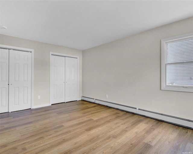 unfurnished bedroom featuring a baseboard radiator, light hardwood / wood-style flooring, and multiple closets