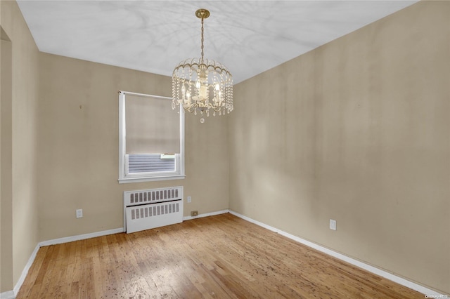 spare room featuring radiator heating unit, wood-type flooring, and an inviting chandelier