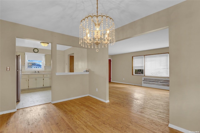 unfurnished dining area with a notable chandelier, radiator heating unit, sink, and light hardwood / wood-style flooring