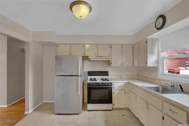 kitchen with sink, backsplash, stainless steel fridge, cream cabinets, and white range with gas cooktop