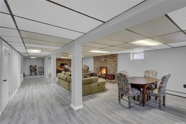 interior space with a brick fireplace, a paneled ceiling, and light hardwood / wood-style flooring