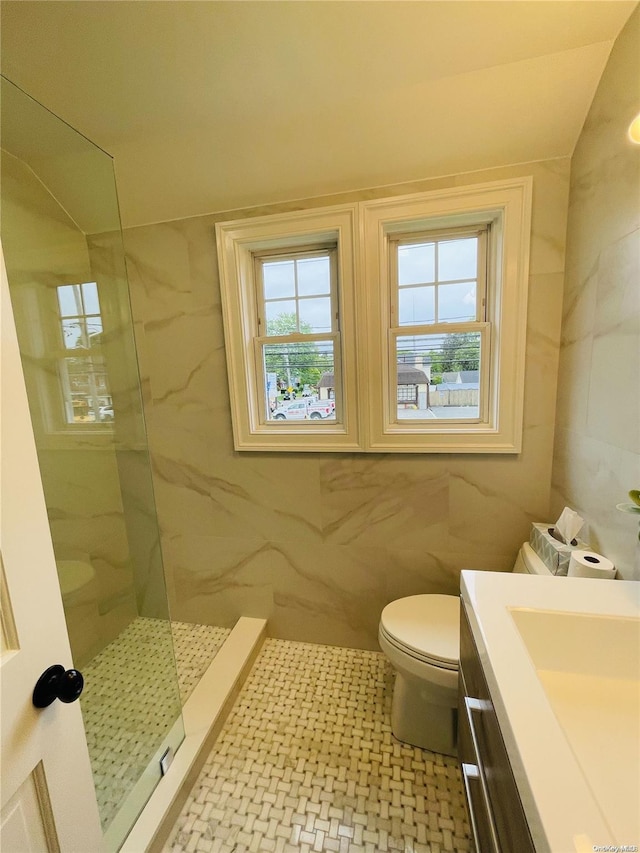 bathroom featuring a tile shower, vanity, toilet, and tile walls