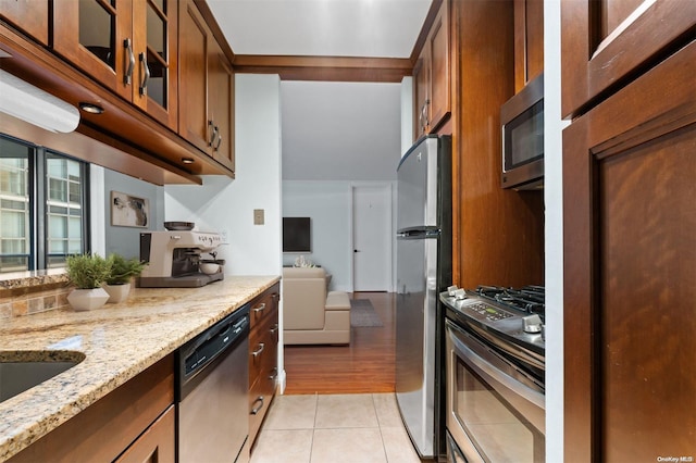 kitchen with appliances with stainless steel finishes, sink, light stone counters, and light tile patterned flooring