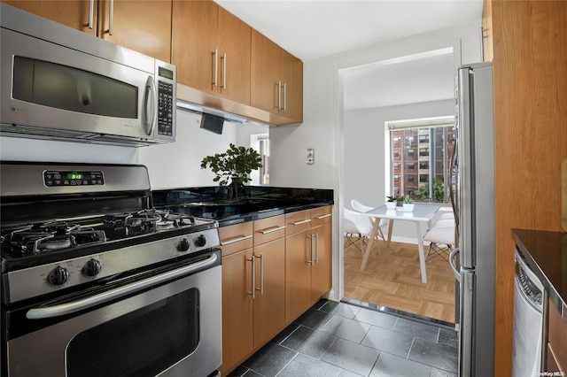 kitchen featuring dark parquet flooring, stainless steel appliances, and dark stone counters