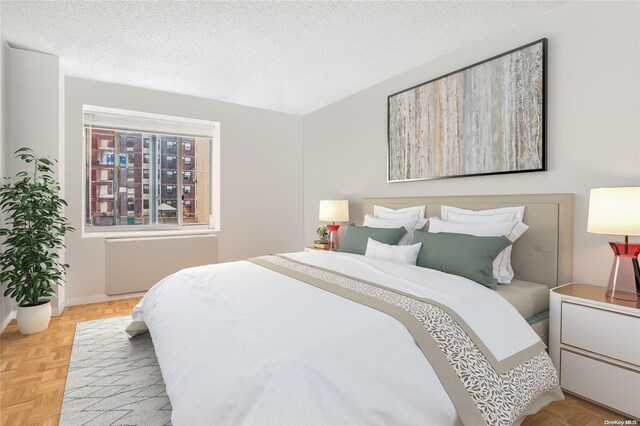 bedroom with radiator heating unit, a textured ceiling, and light parquet flooring