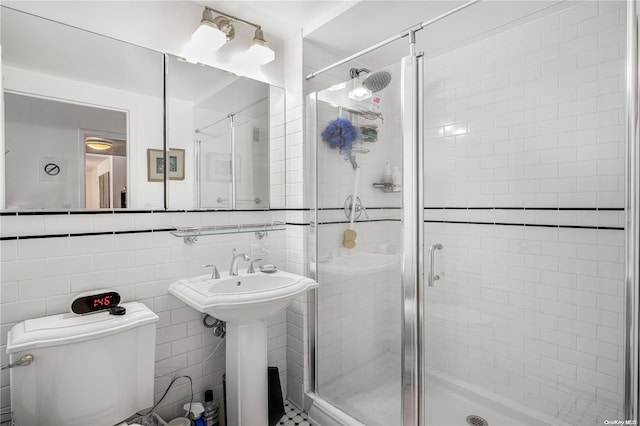 bathroom with sink, toilet, a shower with door, and tile walls