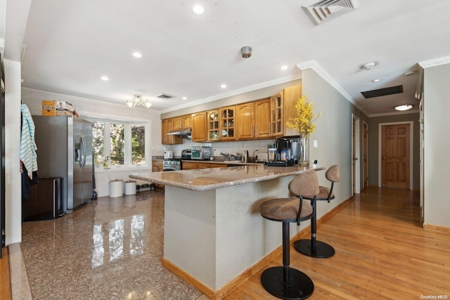 kitchen featuring stainless steel appliances, light stone counters, light wood-type flooring, a kitchen bar, and ornamental molding