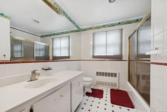 full bathroom featuring combined bath / shower with glass door, radiator, vanity, tile walls, and toilet