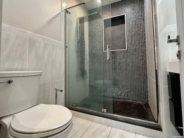 bathroom with tile patterned flooring, a shower with shower door, tile walls, and toilet