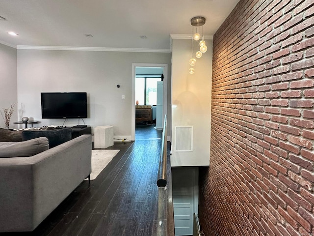 living room with dark wood-type flooring, ornamental molding, and brick wall