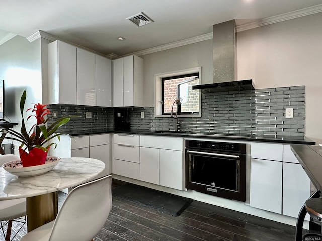 kitchen featuring sink, white cabinets, ornamental molding, black appliances, and wall chimney range hood