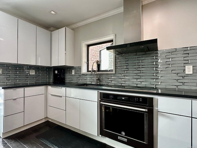 kitchen featuring wall chimney range hood, sink, black appliances, white cabinets, and decorative backsplash