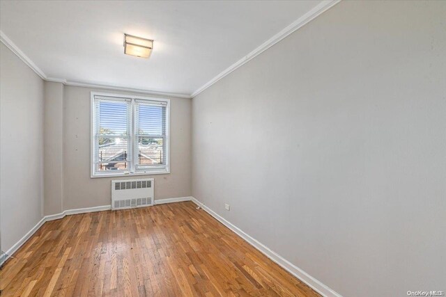 spare room with wood-type flooring, radiator heating unit, and crown molding