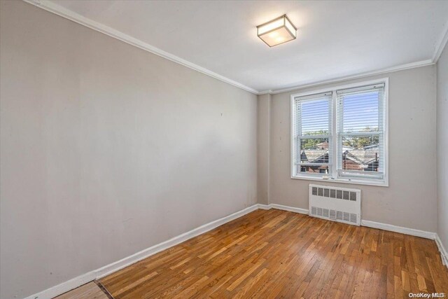 spare room with crown molding, radiator heating unit, and hardwood / wood-style floors