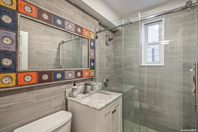 bathroom featuring vanity, toilet, tile walls, and a shower with shower door