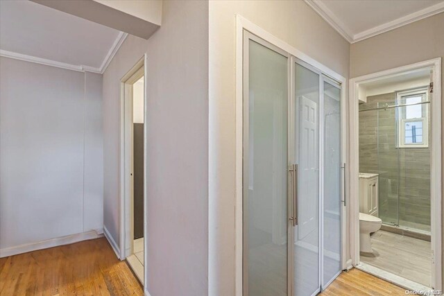 corridor with light wood-type flooring and crown molding