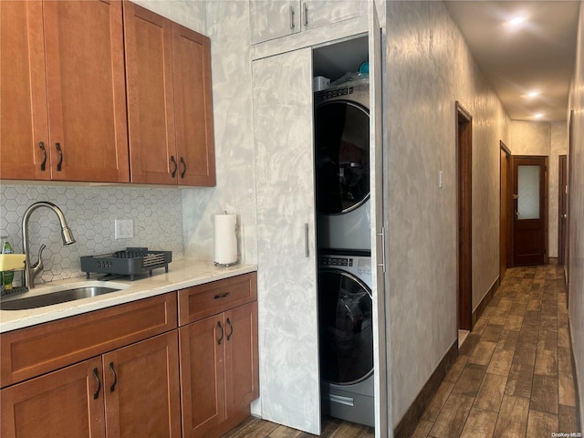 clothes washing area featuring dark hardwood / wood-style floors, stacked washing maching and dryer, and sink