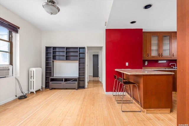 kitchen featuring cooling unit, radiator heating unit, light wood-type flooring, a kitchen bar, and kitchen peninsula