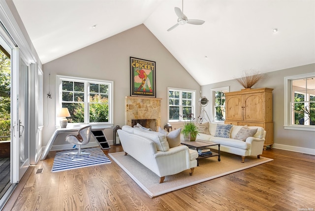 living room featuring a stone fireplace, ceiling fan, hardwood / wood-style floors, and high vaulted ceiling