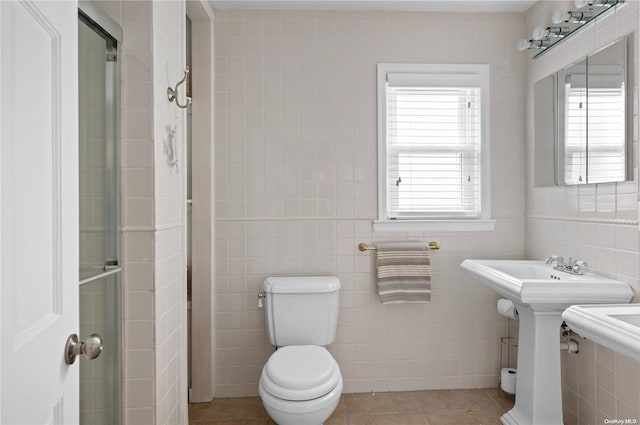 bathroom with toilet, tile patterned floors, tile walls, and sink