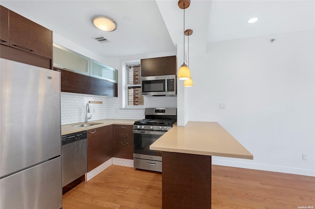 kitchen featuring hanging light fixtures, sink, appliances with stainless steel finishes, light hardwood / wood-style floors, and kitchen peninsula