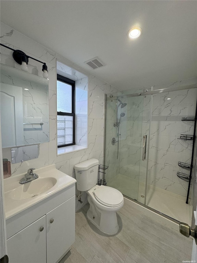 bathroom featuring vanity, a shower with door, toilet, and tile walls